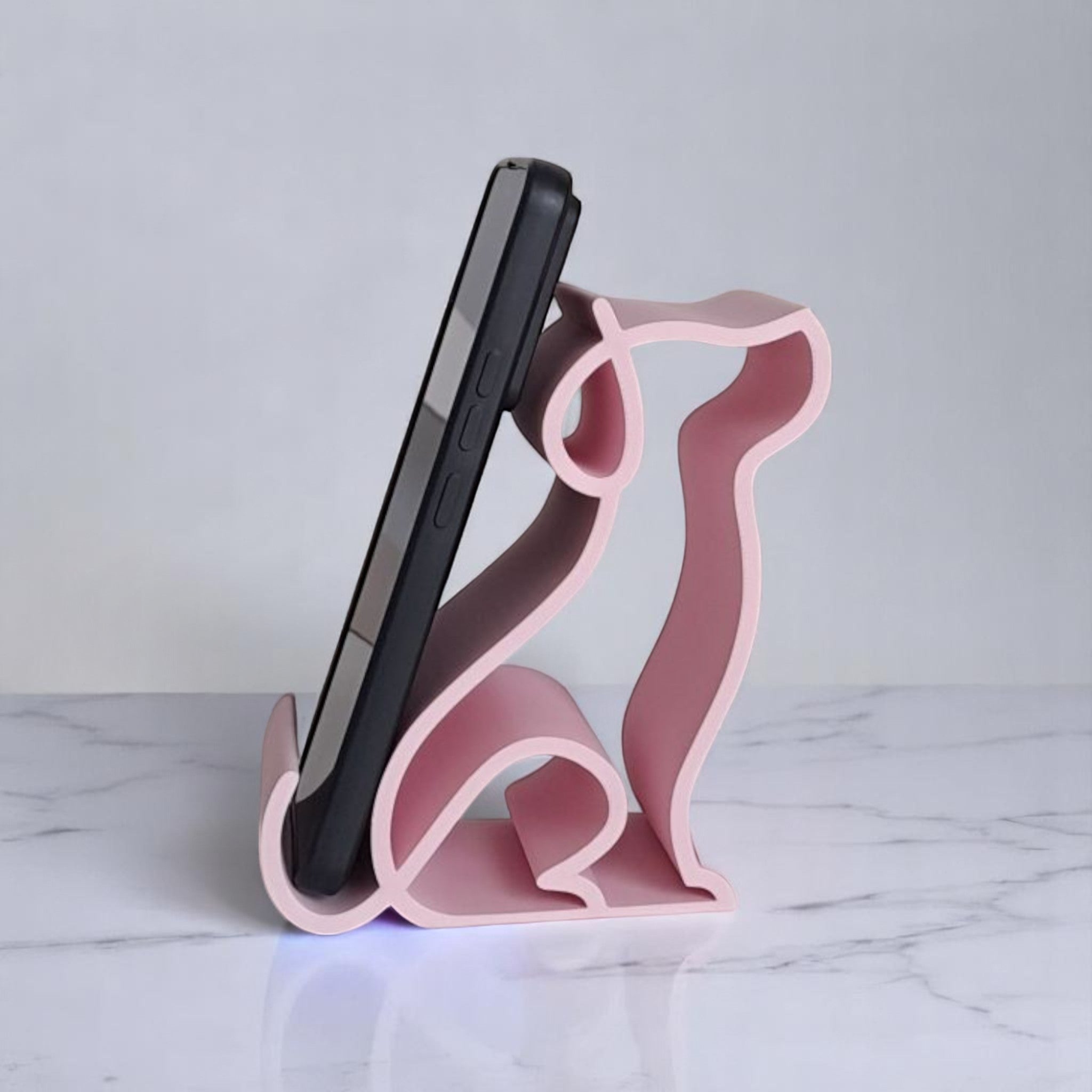 3D printed pink dog-shaped phone holder for desk, used to support a smartphone, tablet, or Kindle, ideal for pet lovers and home office decor