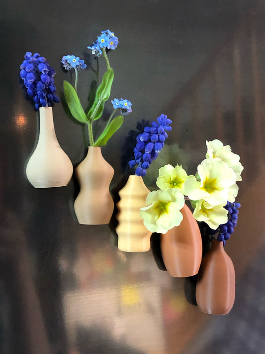 Set of 5 small magnetic mini vases in random earthy brown tones, 3D printed with a modern design, displayed on a fridge holding tiny flowers.