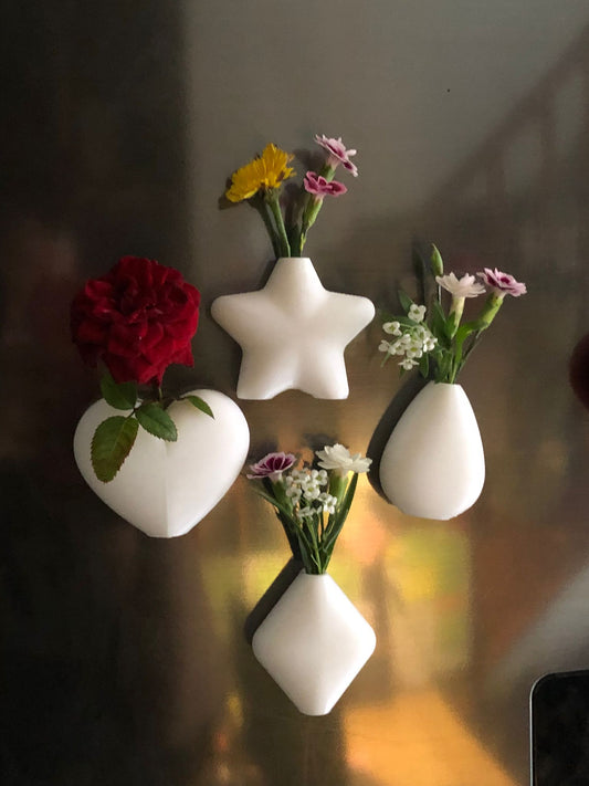 Set of mini magnetic vases in heart, star, diamond, and teardrop shapes, attached to a refrigerator and holding small colorful flowers, displayed in red and white colors.