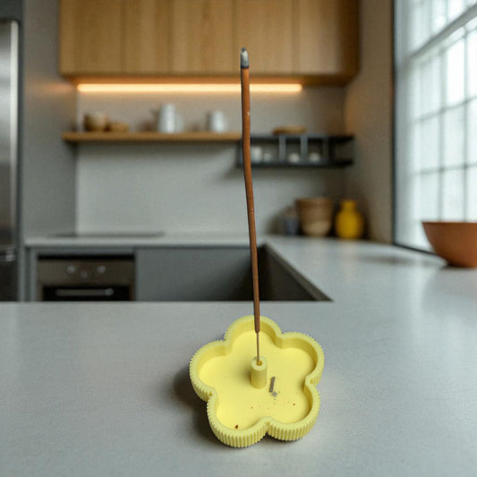 Yellow flower-shaped incense burner with a single stick on a kitchen counter.