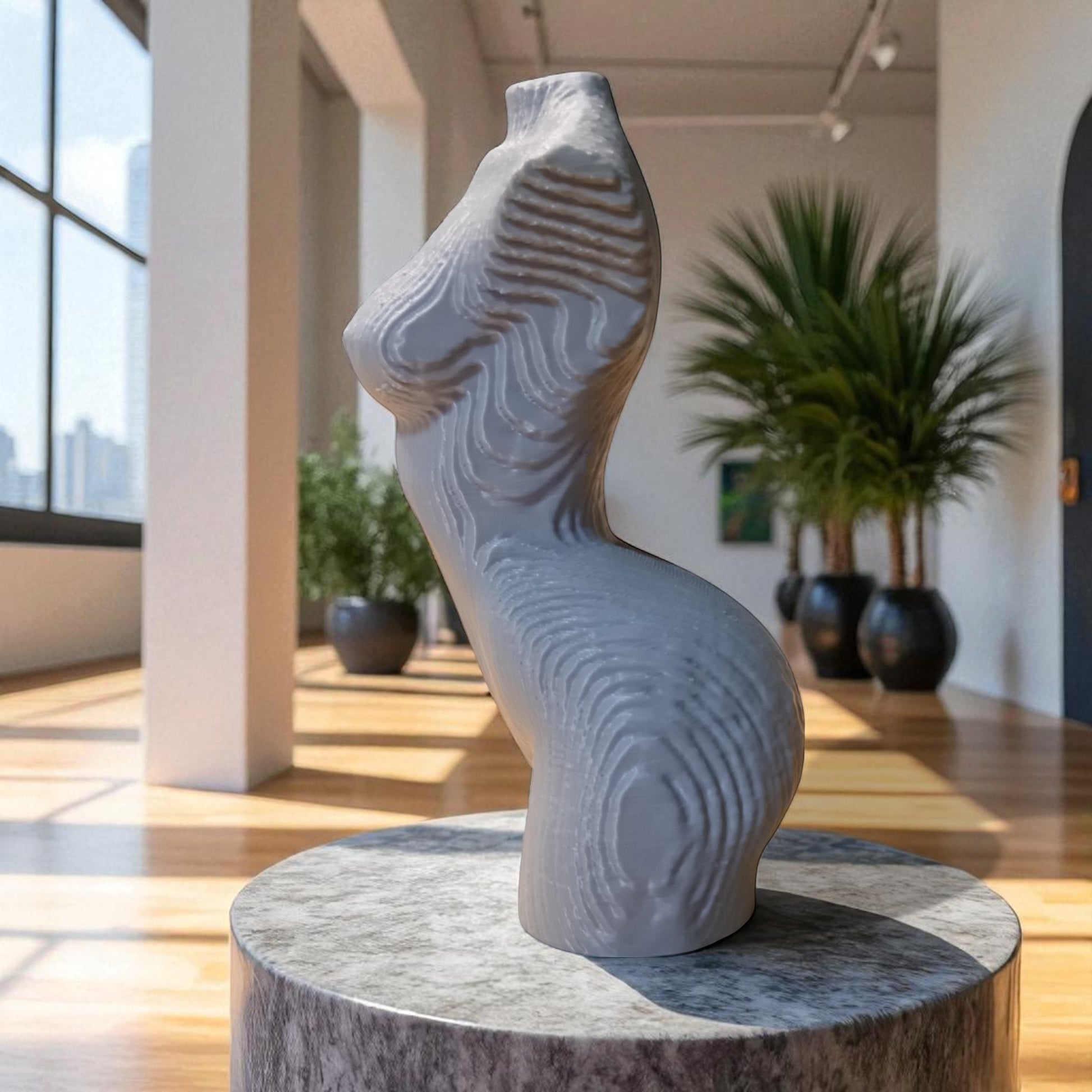 Gray abstract sculpture on a pedestal in a modern indoor setting with plants and large windows.