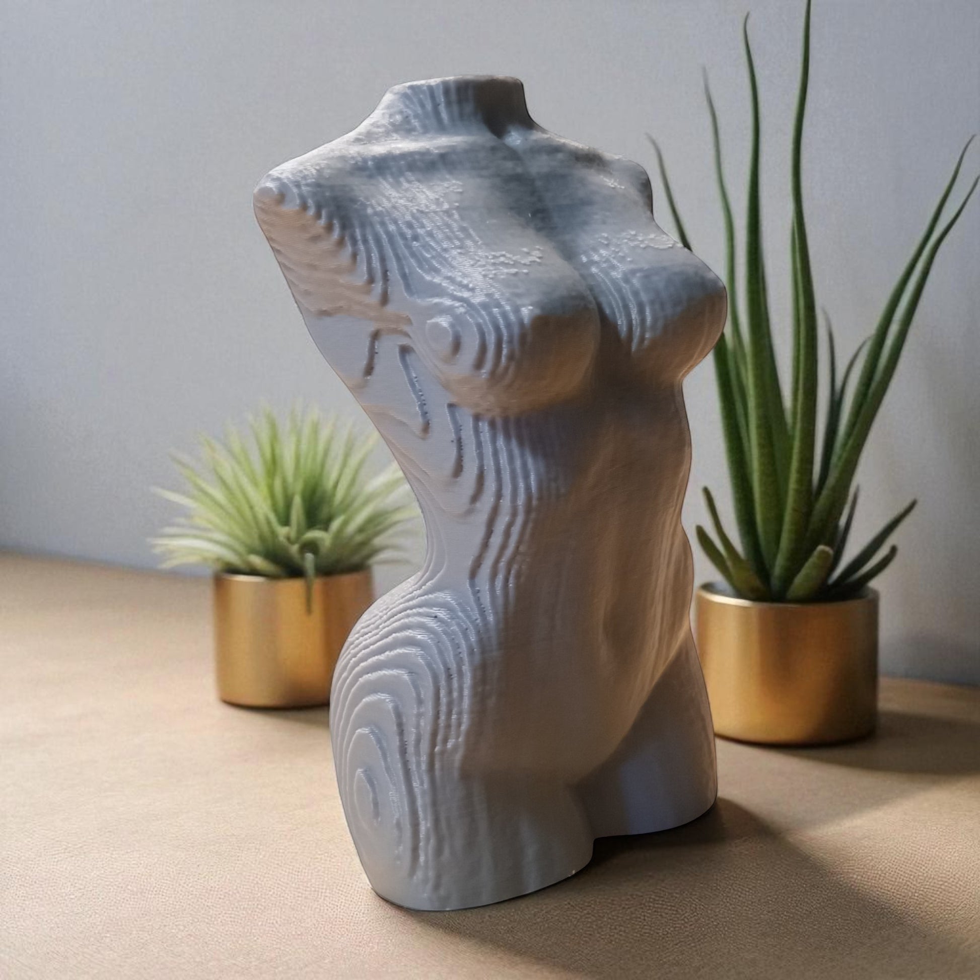Ceramic torso sculpture on a table with two potted plants.