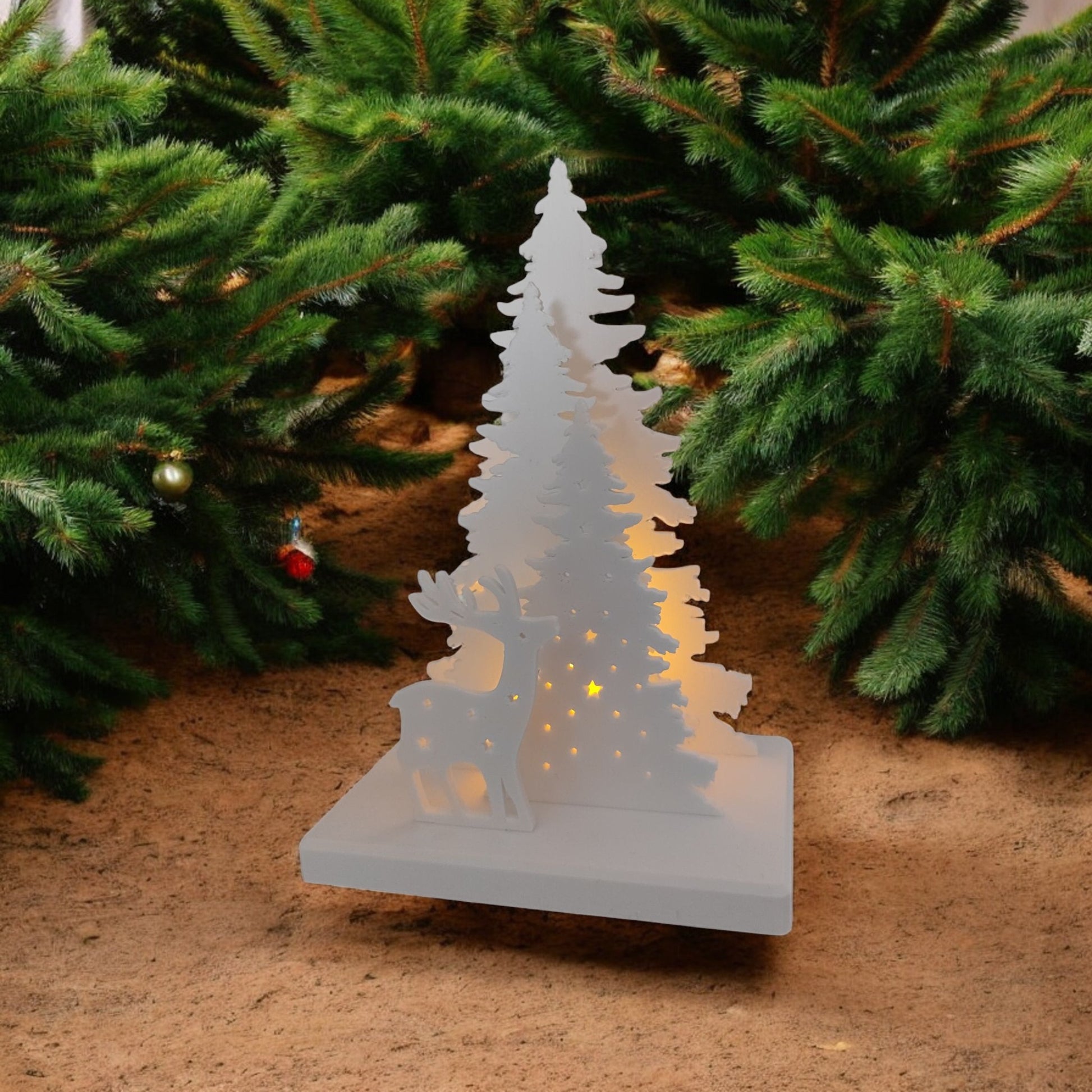 White Christmas reindeer and pine tree LED tealight decoration glowing on table, festive holiday décor for mantel or centerpiece.