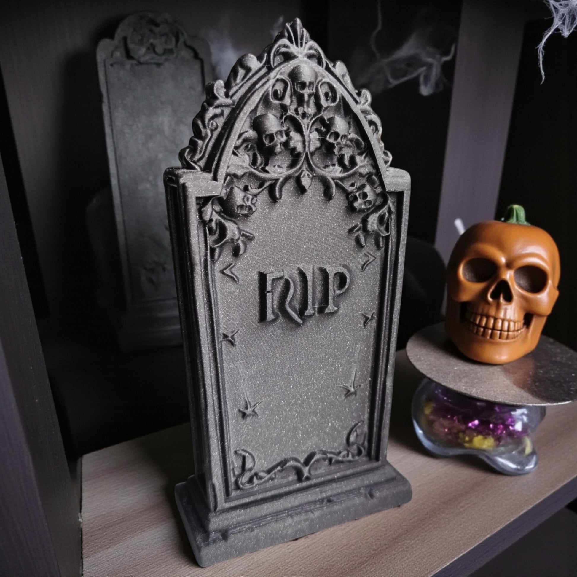 3D printed gothic gravestone with skull details and “RIP” engraving, available in black, grey, and white, shown as Halloween or gothic table decor.
