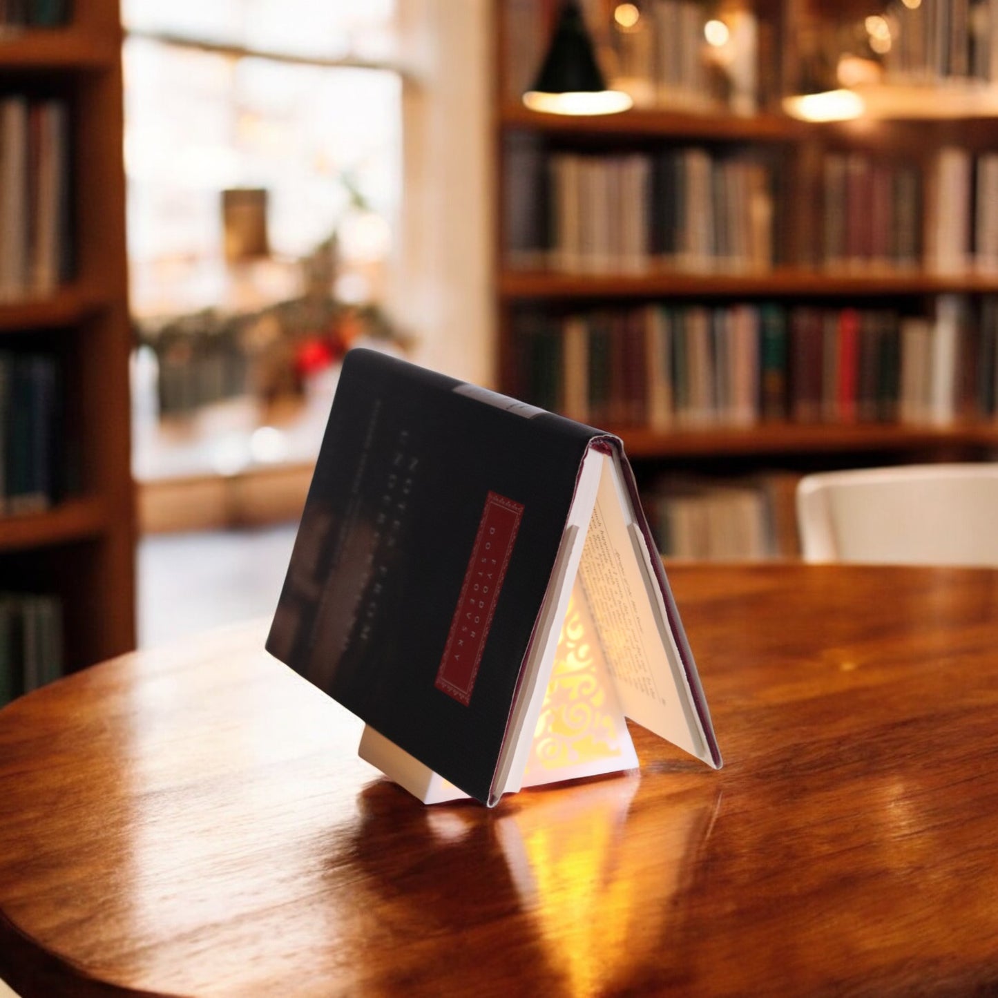 white triangular book stand with an intricate cut-out tree design, displayed on a white surface against a light grey background.