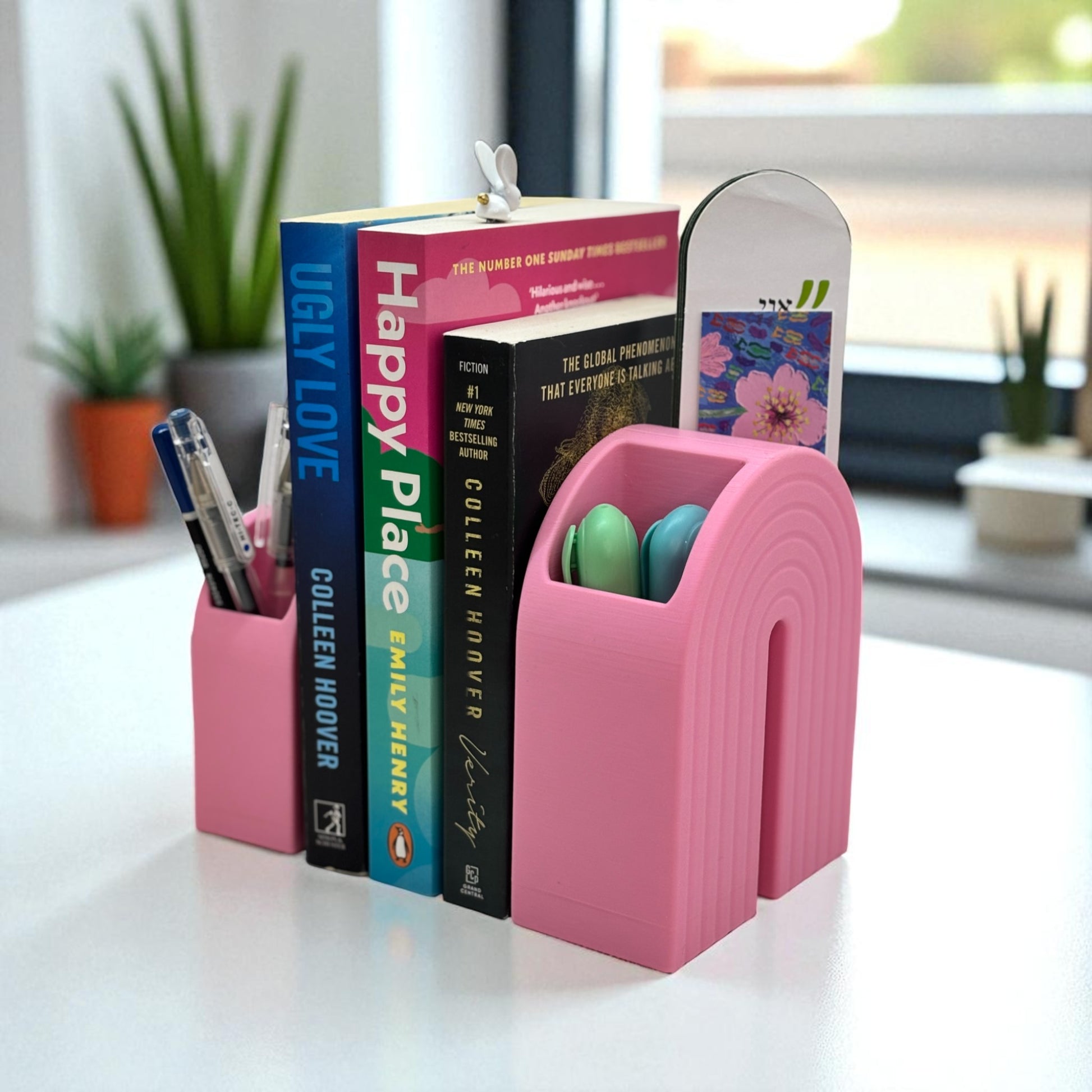 Colorful 3D printed rainbow-shaped organizer used as a bookend, pen holder, and mini vase, displayed in two sizes on a shelf with books, stationery, and dried flowers.