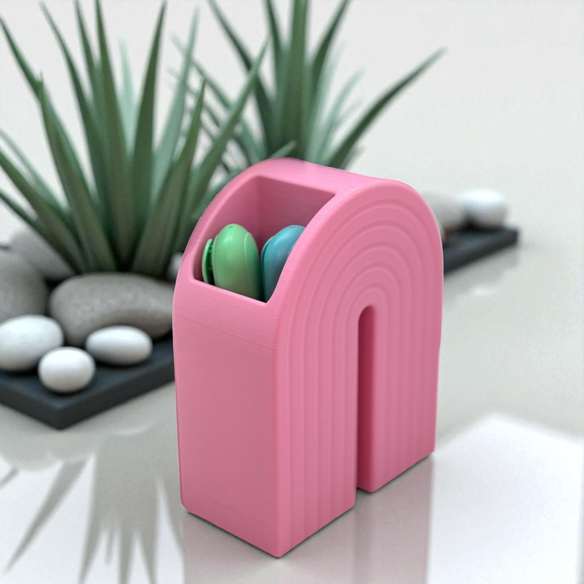 Colorful 3D printed rainbow-shaped organizer used as a bookend, pen holder, and mini vase, displayed in two sizes on a shelf with books, stationery, and dried flowers.
