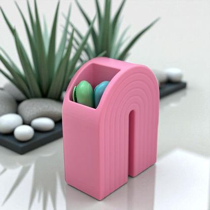 Colorful 3D printed rainbow-shaped organizer used as a bookend, pen holder, and mini vase, displayed in two sizes on a shelf with books, stationery, and dried flowers.