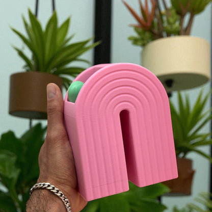 Colorful 3D printed rainbow-shaped organizer used as a bookend, pen holder, and mini vase, displayed in two sizes on a shelf with books, stationery, and dried flowers.