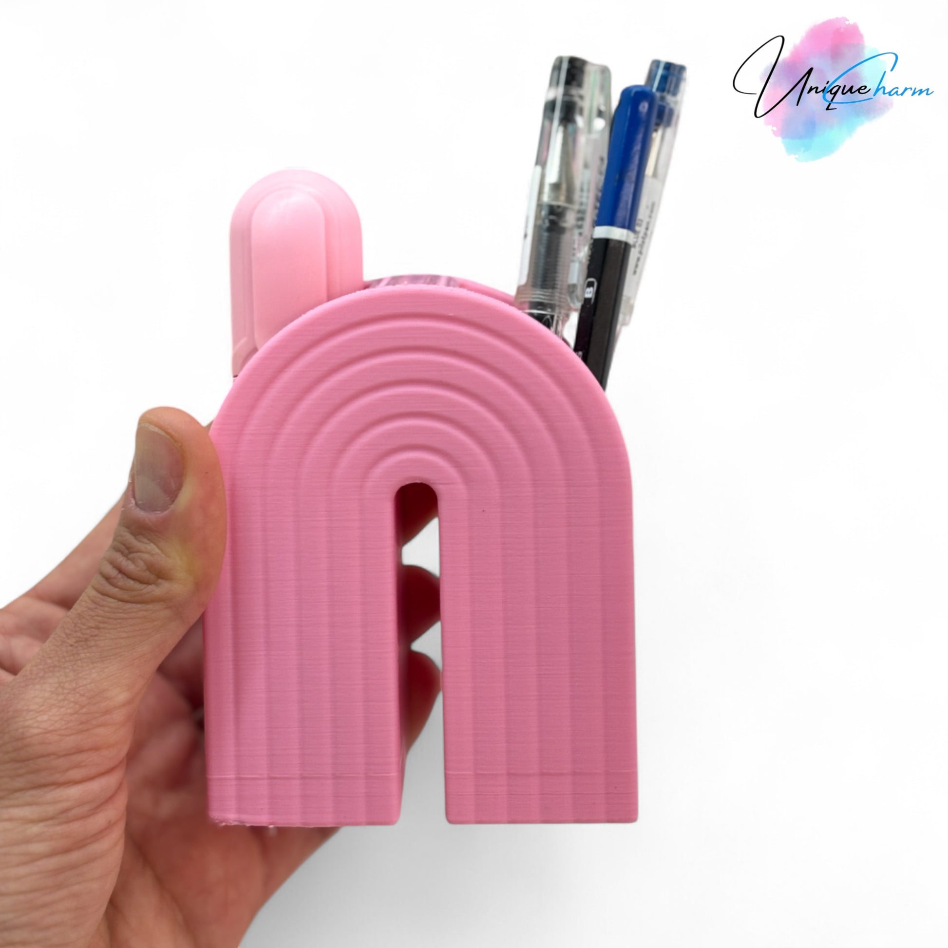 Colorful 3D printed rainbow-shaped organizer used as a bookend, pen holder, and mini vase, displayed in two sizes on a shelf with books, stationery, and dried flowers.
