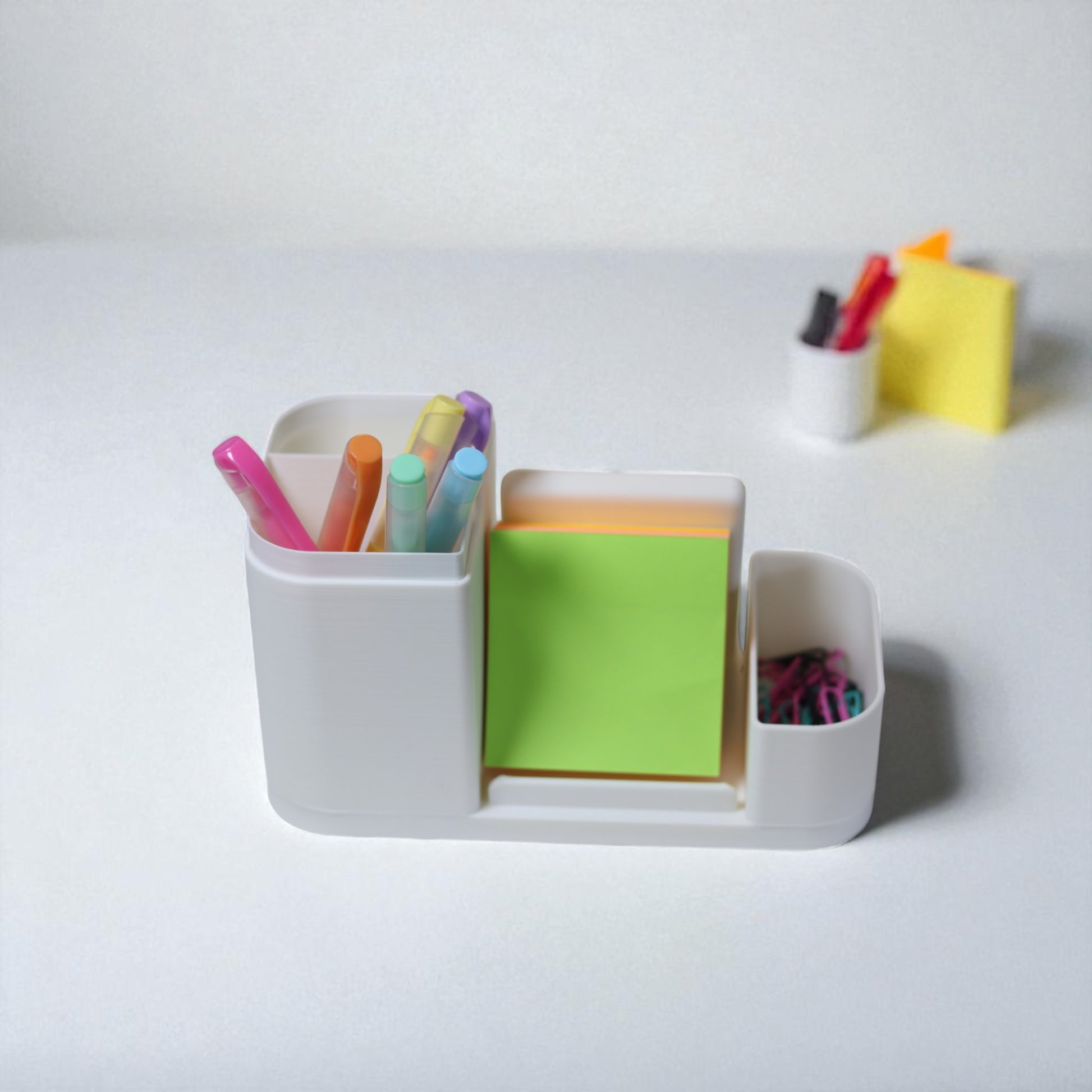 Kids desk organiser with phone stand, pencil/brush holder and sticky-note slot, 20×11×10 cm—white.Front view: organiser holding markers, smartphone in stand, and 3×3 sticky notes—back-to-school desk tidy.