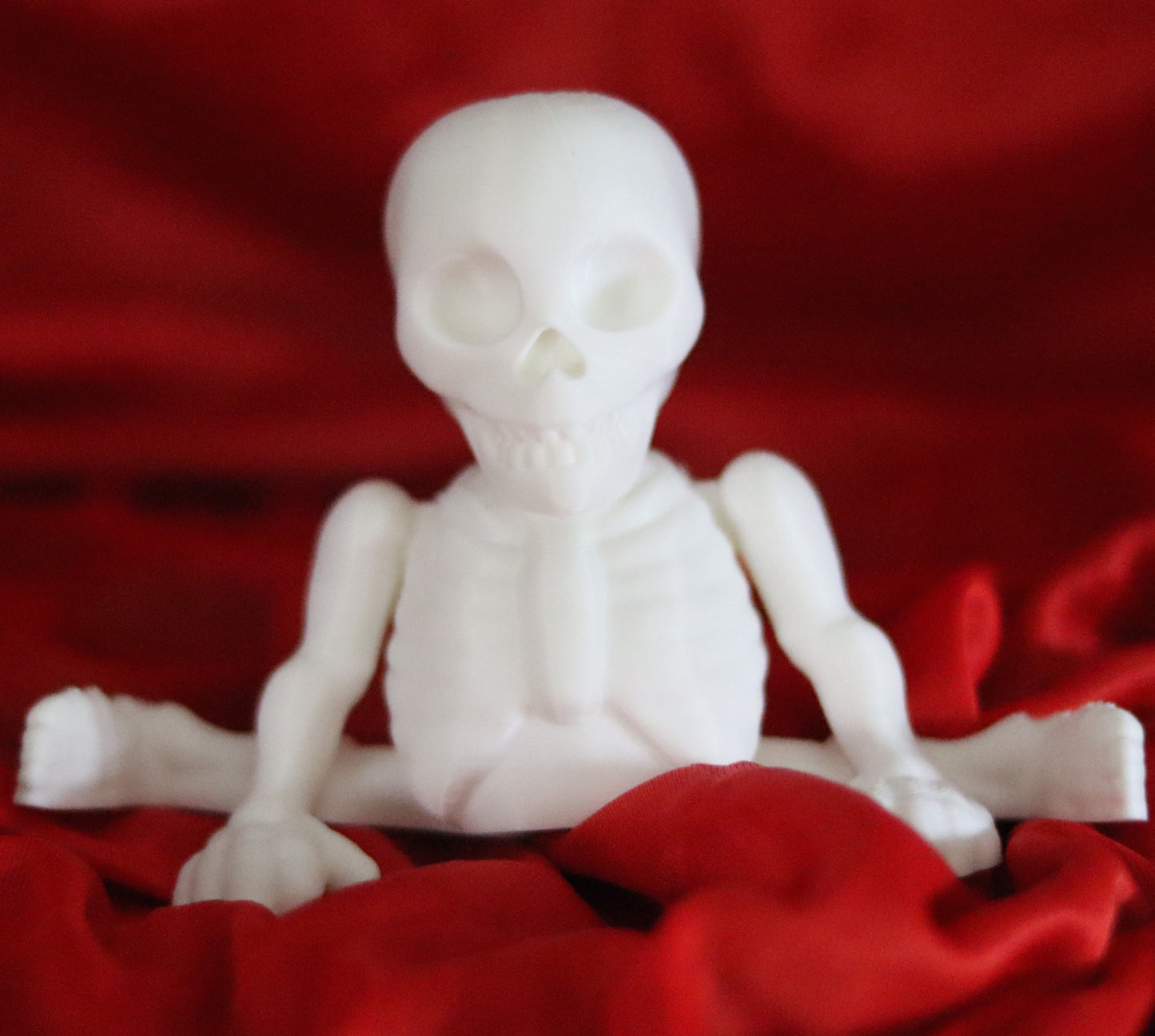 white 3d-printed skeleton figurine raising both arms on a yellow background; spooky-cute desk buddy with lightly poseable joints.