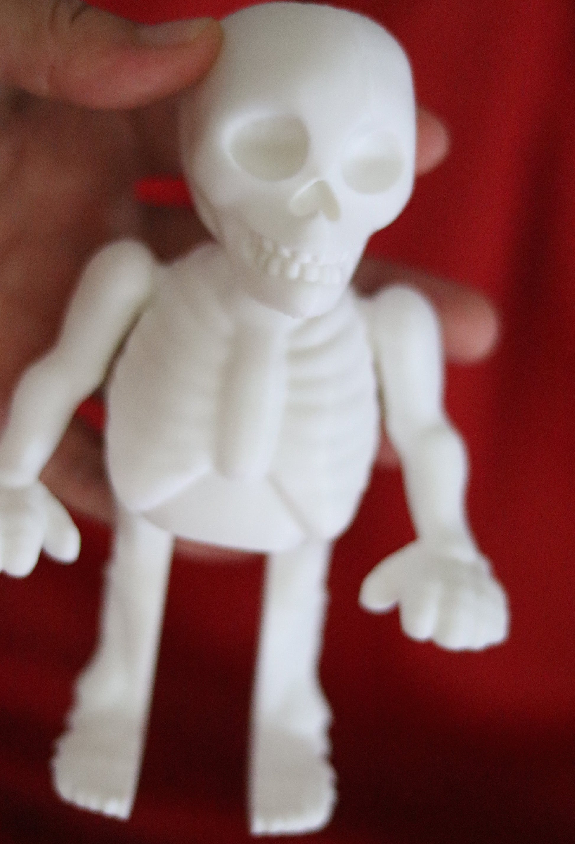 White 3D-printed skeleton figurine raising both arms on a yellow background; spooky-cute desk buddy with lightly poseable joints.