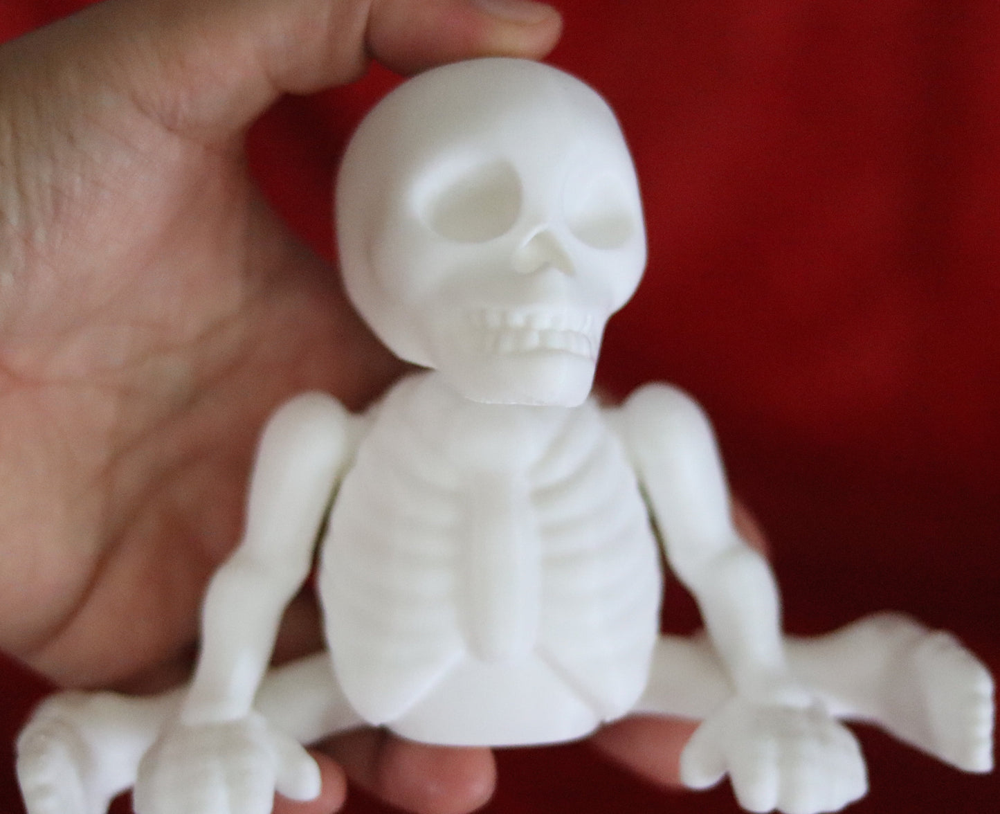 white 3d-printed skeleton figurine raising both arms on a yellow background; spooky-cute desk buddy with lightly poseable joints.