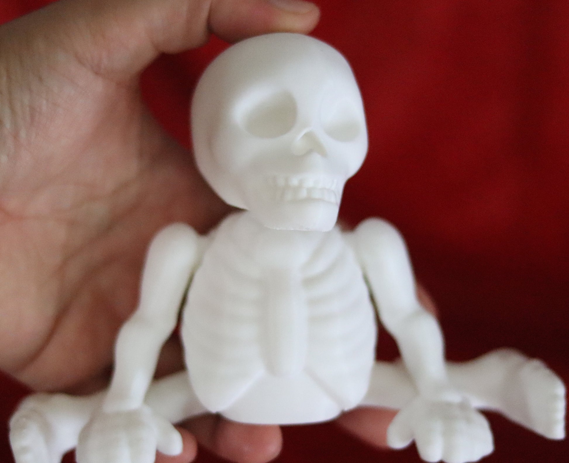 White 3D-printed skeleton figurine raising both arms on a yellow background; spooky-cute desk buddy with lightly poseable joints.