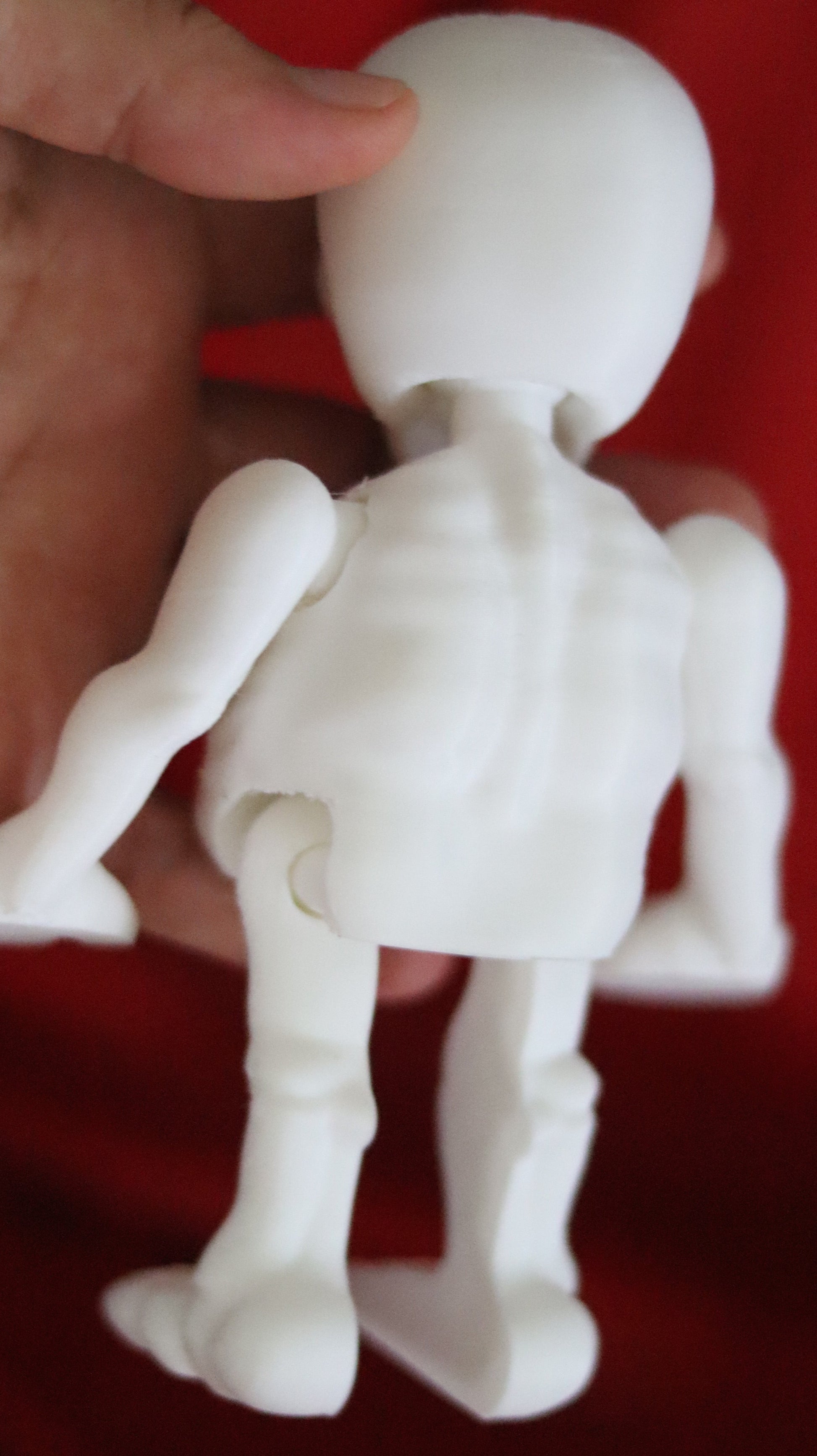 White 3D-printed skeleton figurine raising both arms on a yellow background; spooky-cute desk buddy with lightly poseable joints.