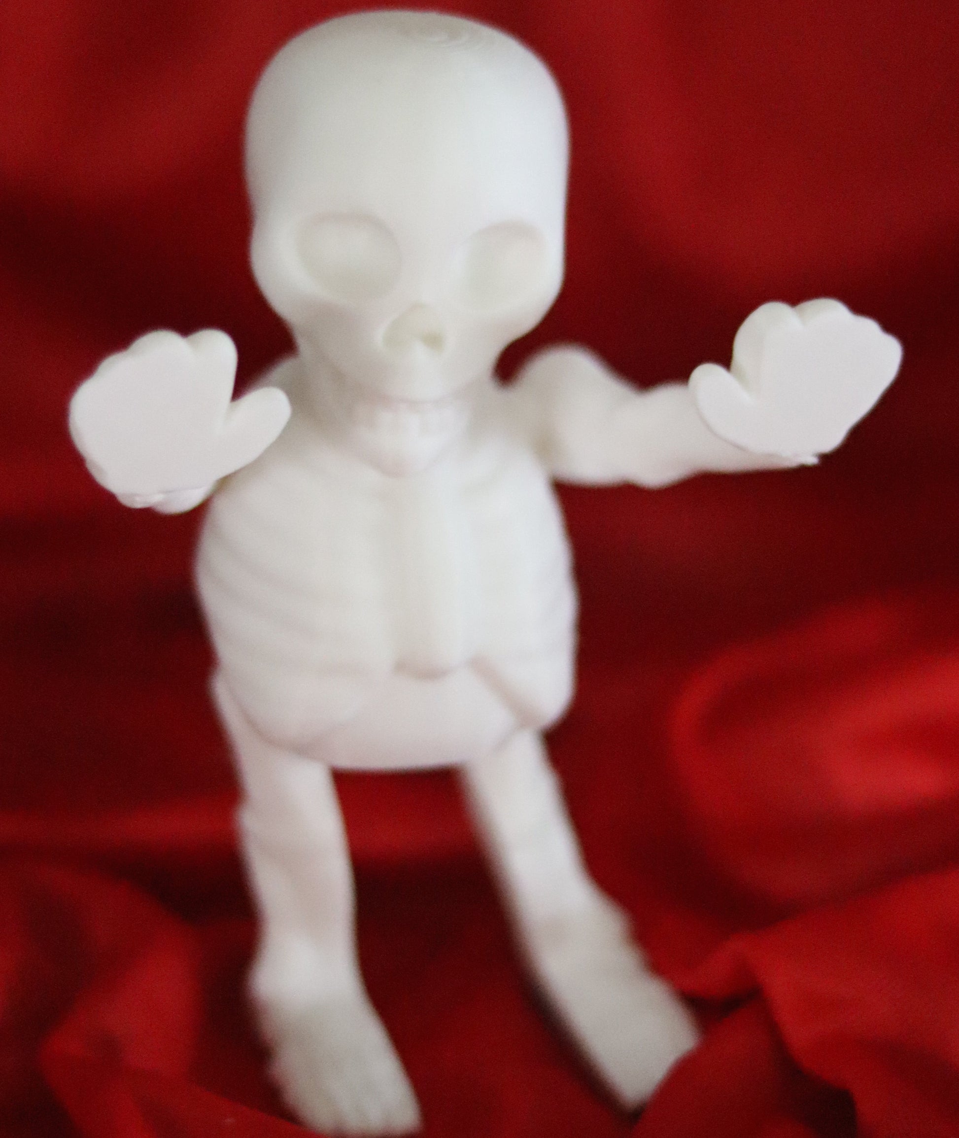 White 3D-printed skeleton figurine raising both arms on a yellow background; spooky-cute desk buddy with lightly poseable joints.
