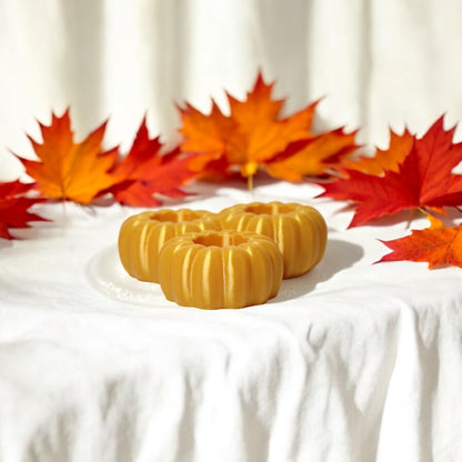 Set of three pumpkin tealight holders (16×14×5.5 cm), neutral colours, showing option with LED tealights lit, displayed on fall tabletop with autumn leaves.