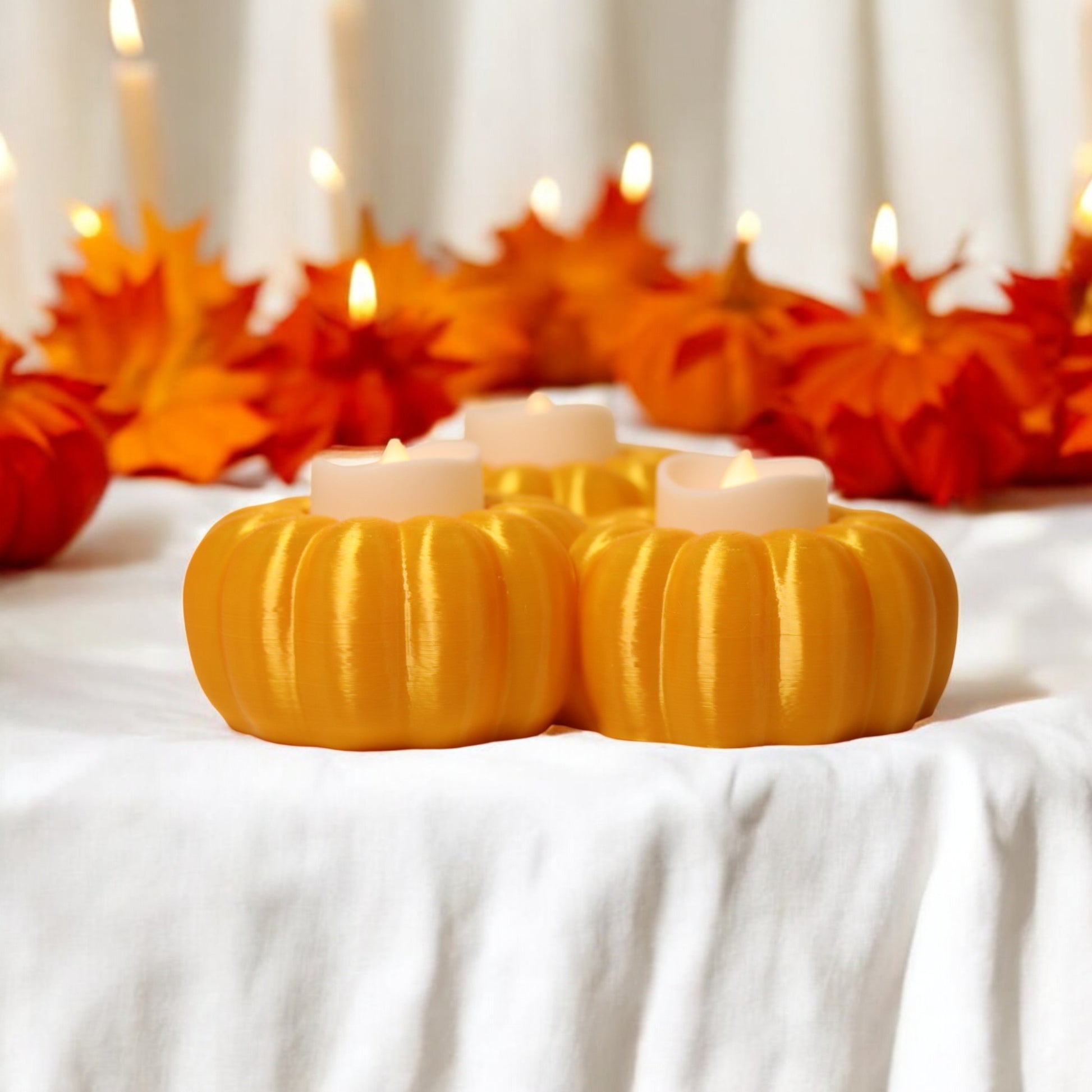 Set of three pumpkin tealight holders (16×14×5.5 cm), neutral colours, showing option with LED tealights lit, displayed on fall tabletop with autumn leaves.