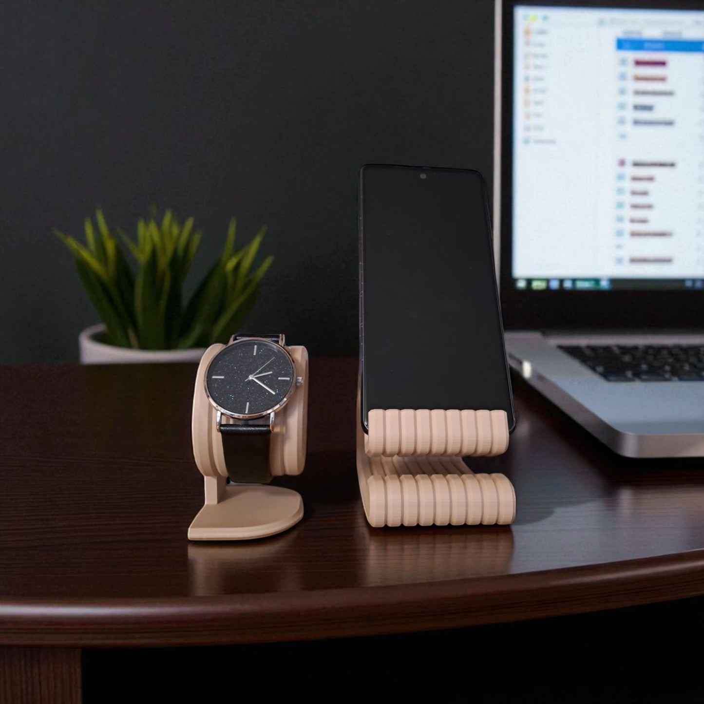 wooden watch stand and phone stand on a desk with a laptop and plant in the background