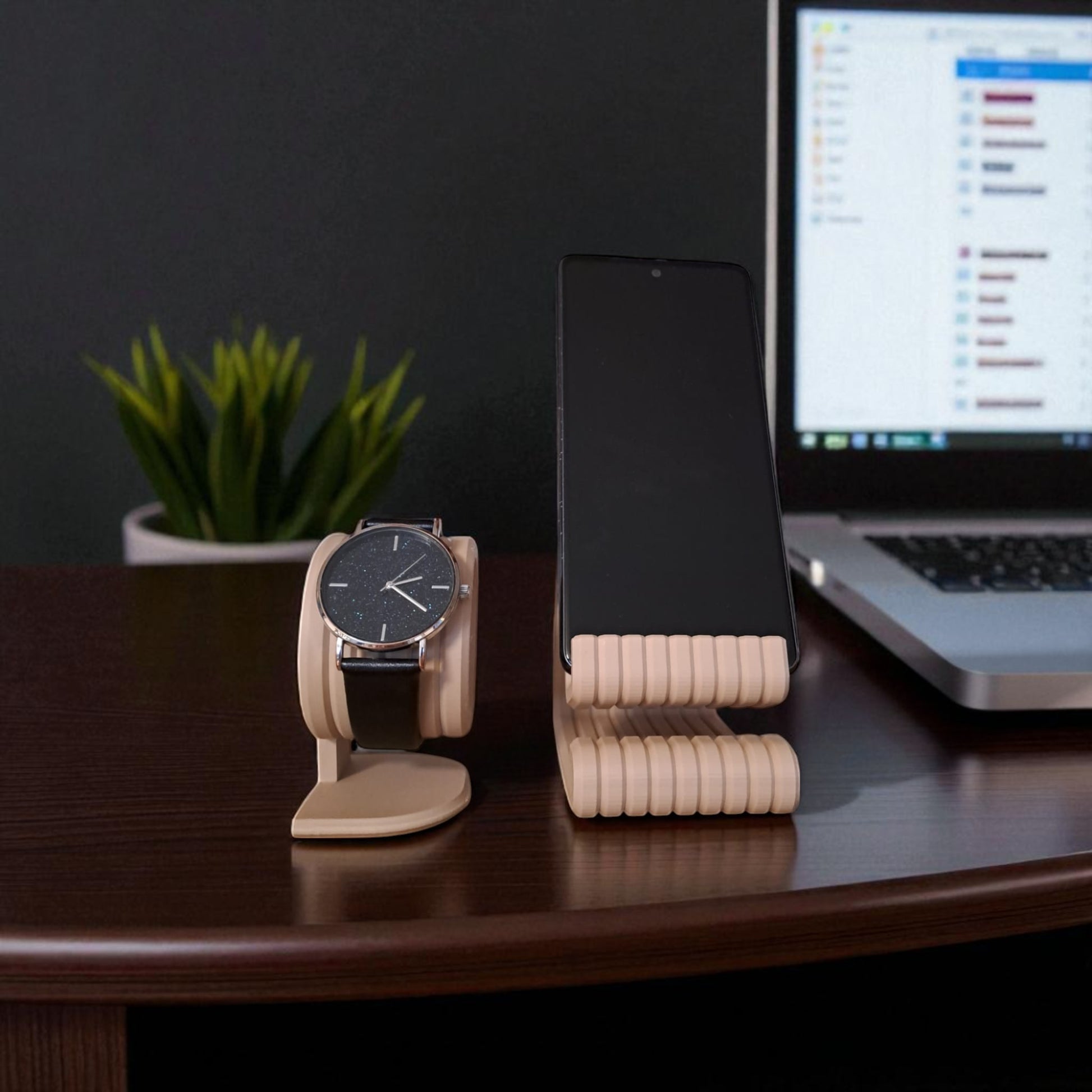 Wooden watch stand and phone stand on a desk with a laptop and plant in the background