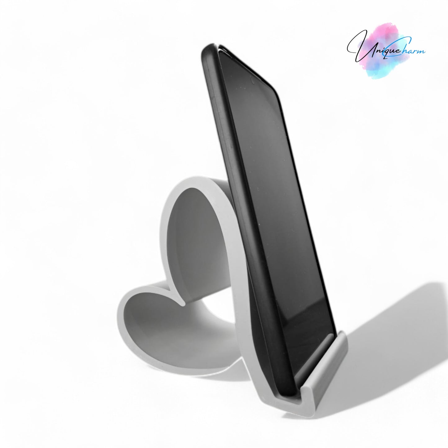 heart-shaped universal phone and kindle holder in an elegant design, securely holding a smartphone on a desk. stylish and versatile stand suitable for all phones, kindles, and small tablets, perfect for hands-free viewing