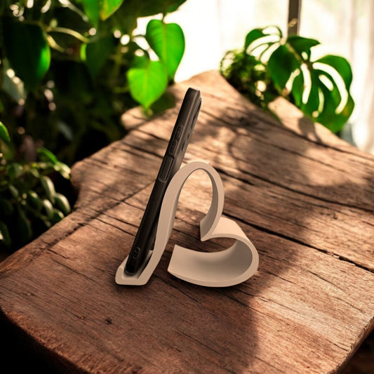 Heart-shaped universal phone and Kindle holder in an elegant design, securely holding a smartphone on a desk. Stylish and versatile stand suitable for all phones, Kindles, and small tablets, perfect for hands-free viewing