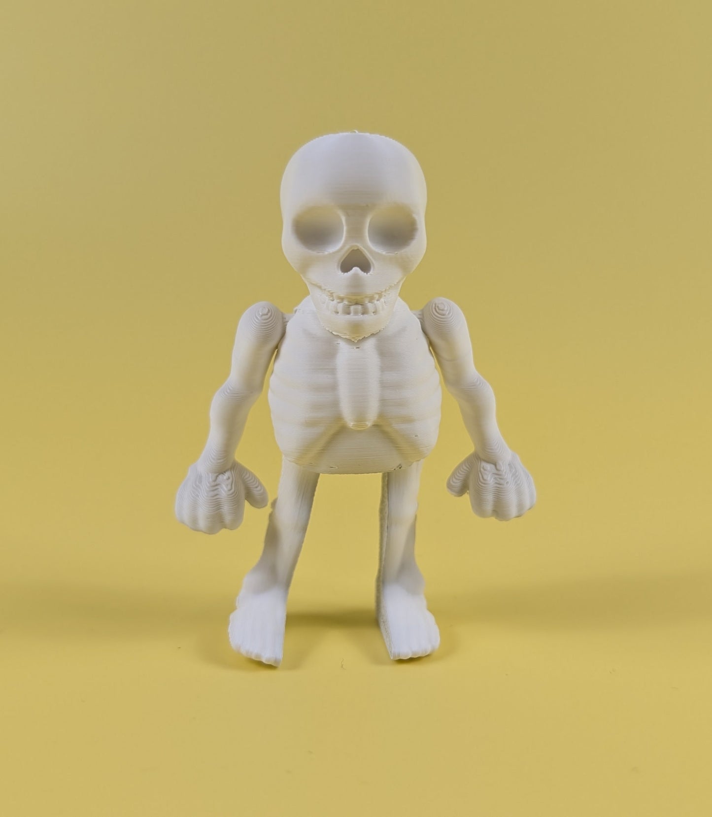 white 3d-printed skeleton figurine raising both arms on a yellow background; spooky-cute desk buddy with lightly poseable joints.