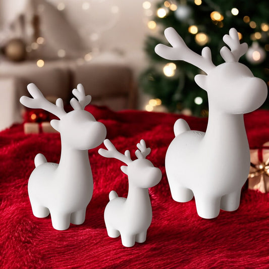 White ceramic reindeer figurines on a red surface with a blurred Christmas tree in the background