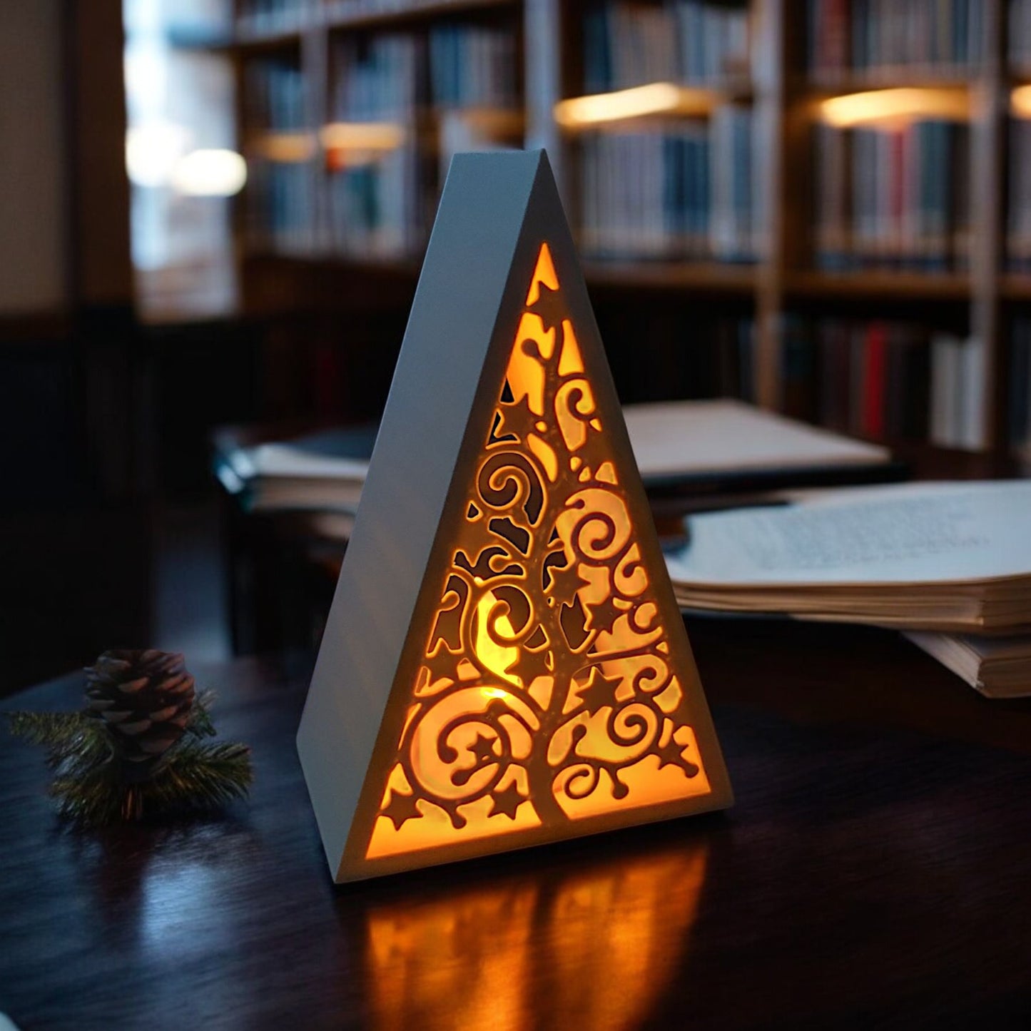white triangular book stand with an intricate cut-out tree design, displayed on a white surface against a light grey background.