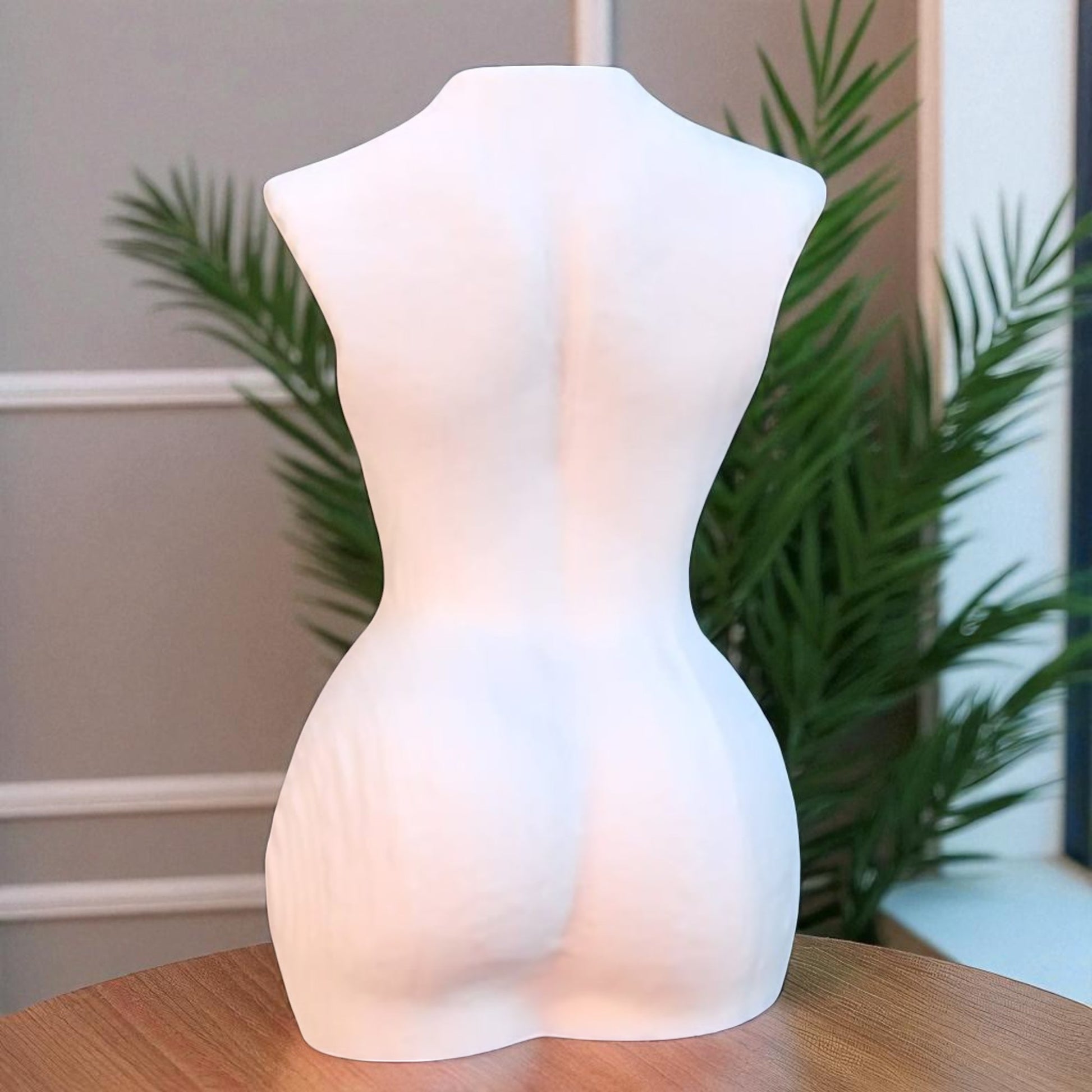 White mannequin torso on a wooden surface with plants in the background