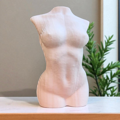 Gray abstract sculpture on a pedestal in a modern indoor setting with plants and large windows.