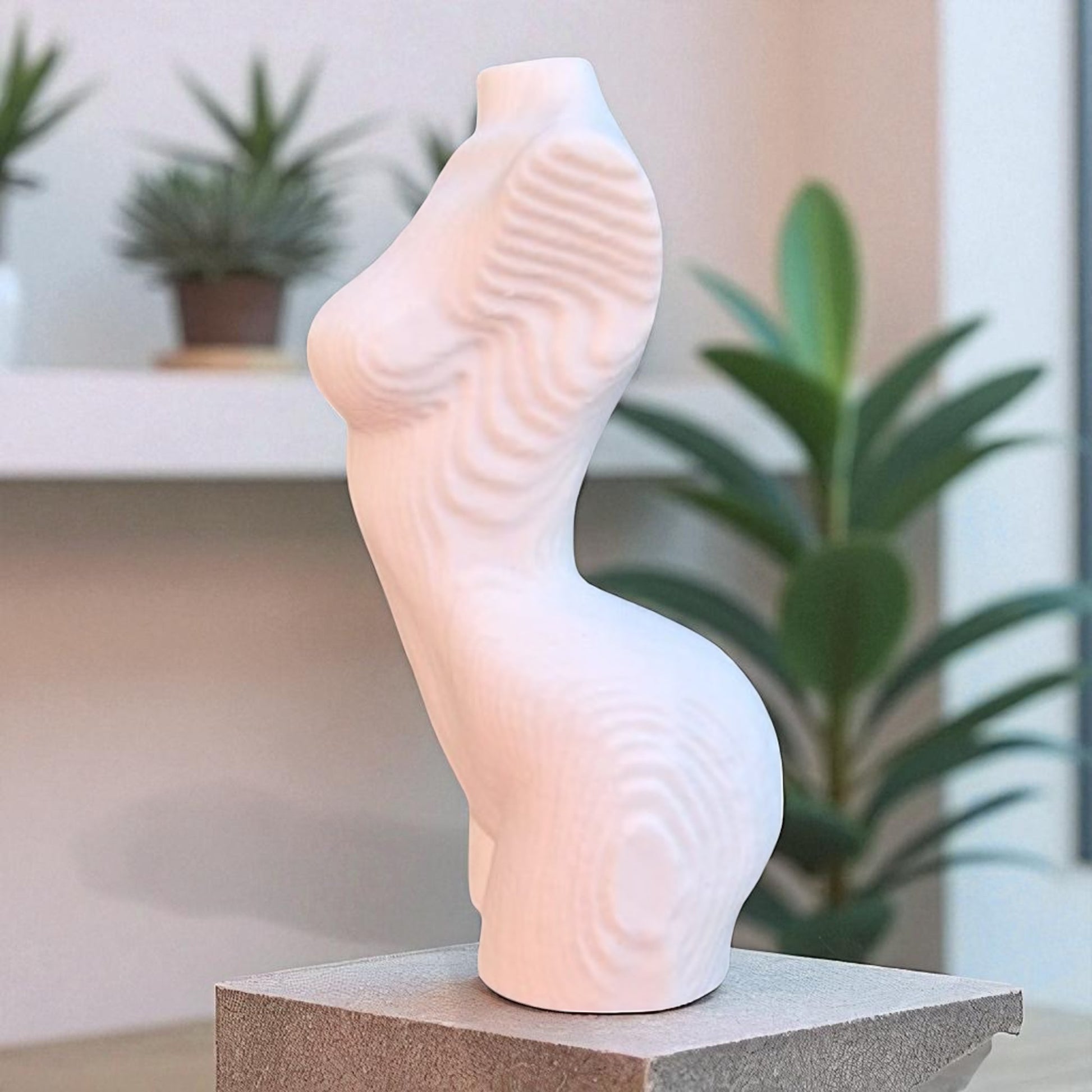 Gray abstract sculpture on a pedestal in a modern indoor setting with plants and large windows.