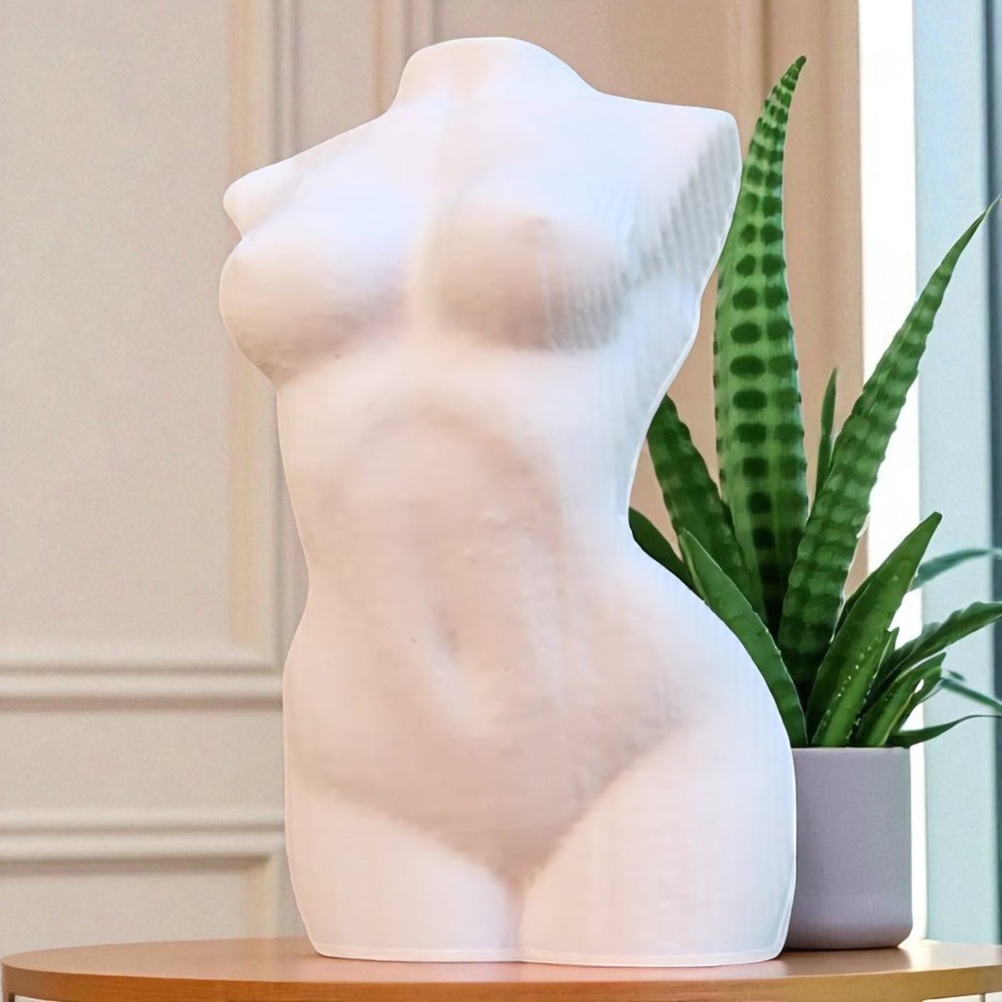 White sculpture of a female torso on a wooden surface with a potted plant.