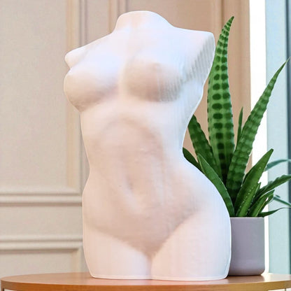 White sculpture of a female torso on a wooden surface with a potted plant.