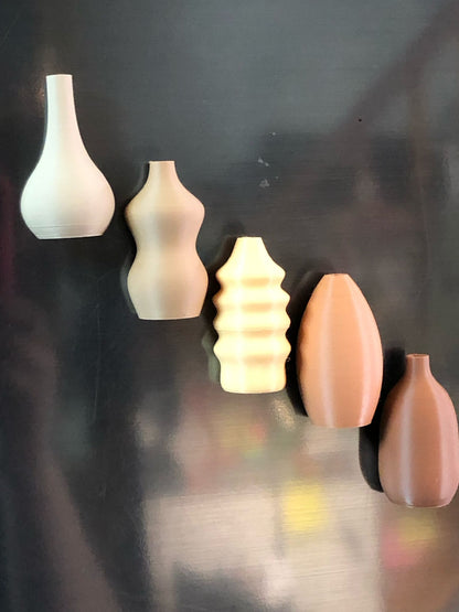 Set of 5 small magnetic mini vases in random earthy brown tones, 3D printed with a modern design, displayed on a fridge holding tiny flowers.

