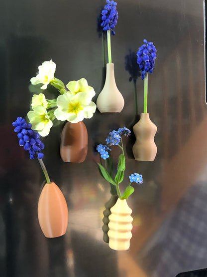 Set of 5 small magnetic mini vases in random earthy brown tones, 3D printed with a modern design, displayed on a fridge holding tiny flowers.

