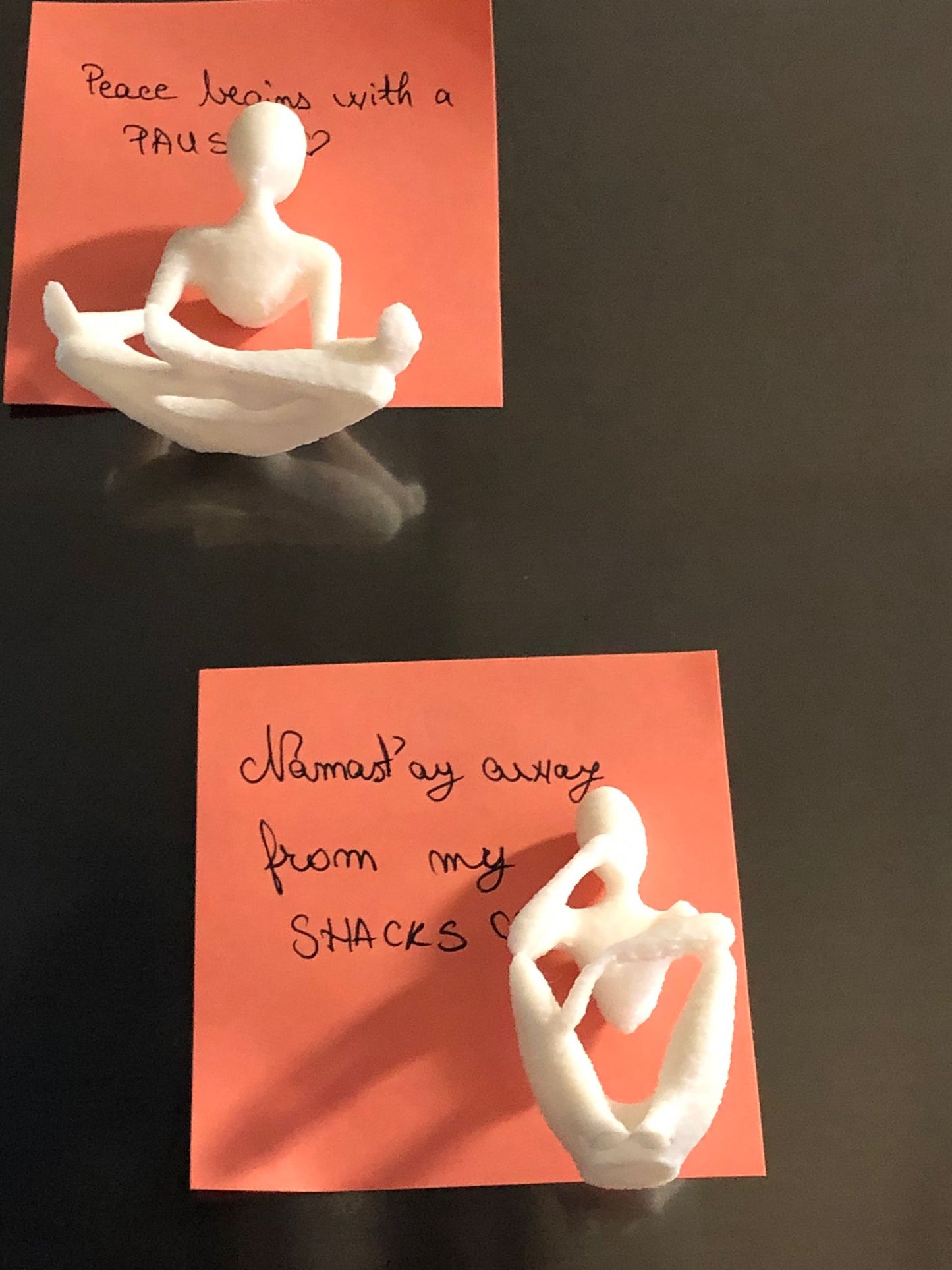 set of two white 3d printed fridge magnets shaped like minimalist faceless human figures in yoga and meditation poses, displayed on a metallic surface.