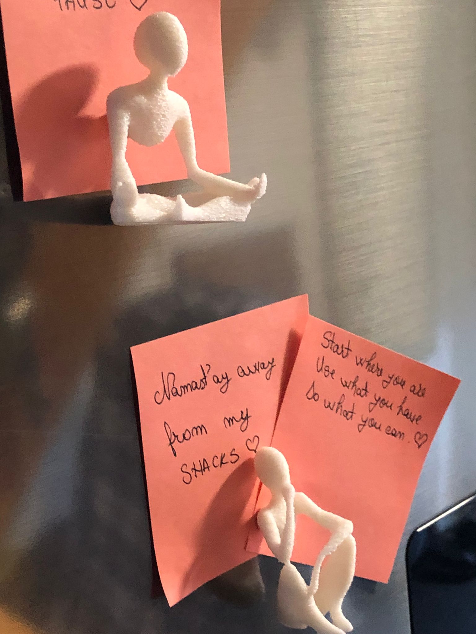 Set of two white 3D printed fridge magnets shaped like minimalist faceless human figures in yoga and meditation poses, displayed on a metallic surface.