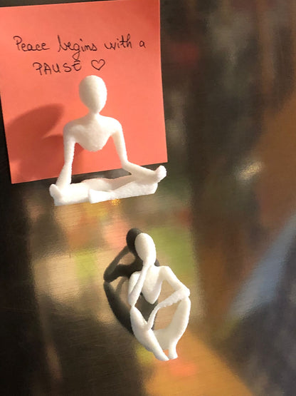 Set of two white 3D printed fridge magnets shaped like minimalist faceless human figures in yoga and meditation poses, displayed on a metallic surface.