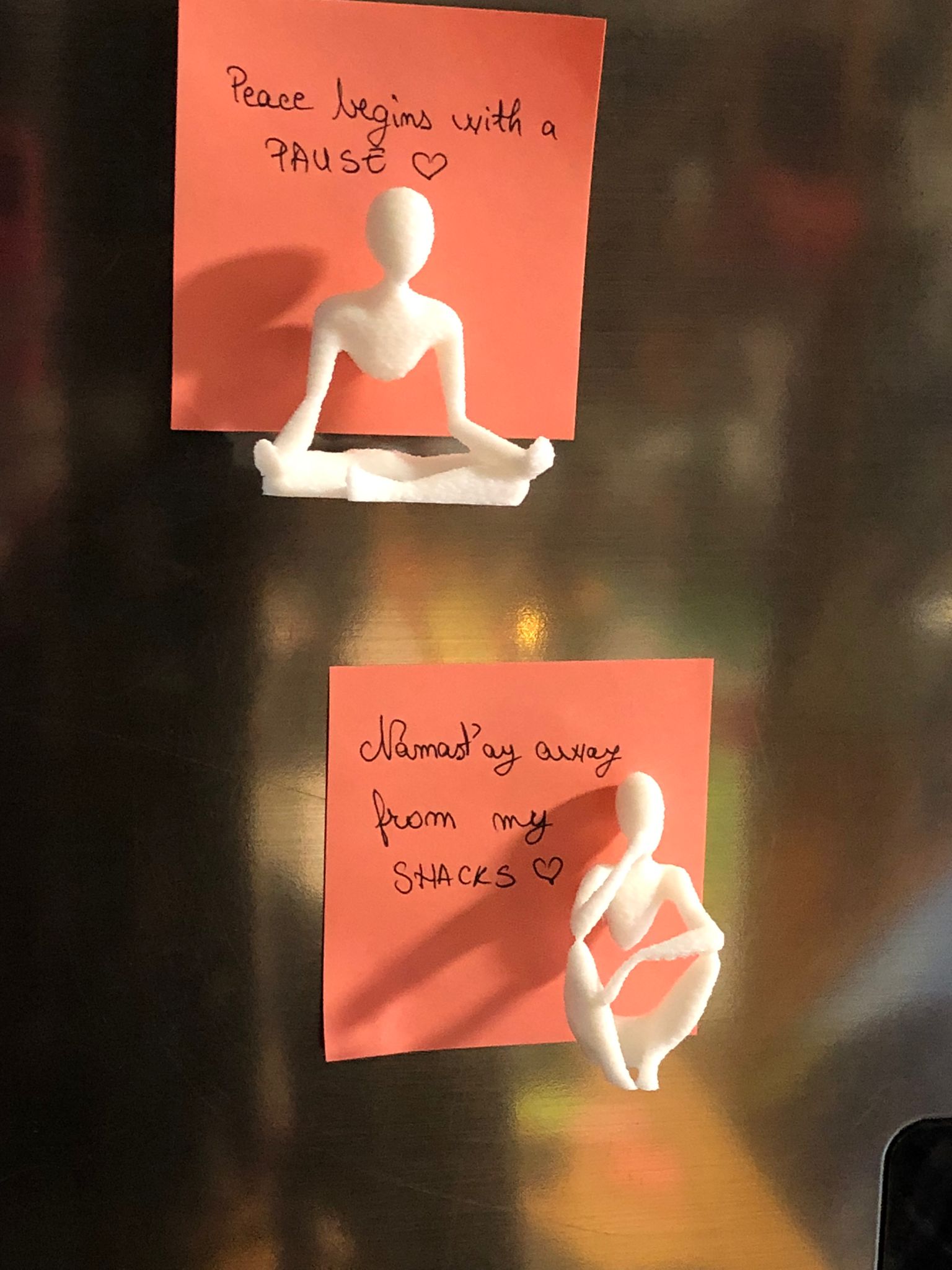 Set of two white 3D printed fridge magnets shaped like minimalist faceless human figures in yoga and meditation poses, displayed on a metallic surface.