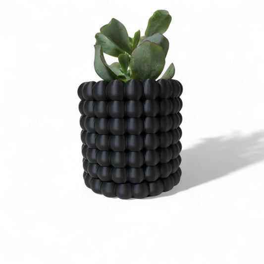 Modern black wall-mounted planter with a bubble texture design, holding a green succulent plant. Includes mounting bracket for screws or adhesive and a built-in water tray.