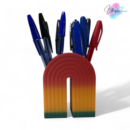 Colorful 3D printed rainbow-shaped organizer used as a bookend, pen holder, and mini vase, displayed in two sizes on a shelf with books, stationery, and dried flowers.