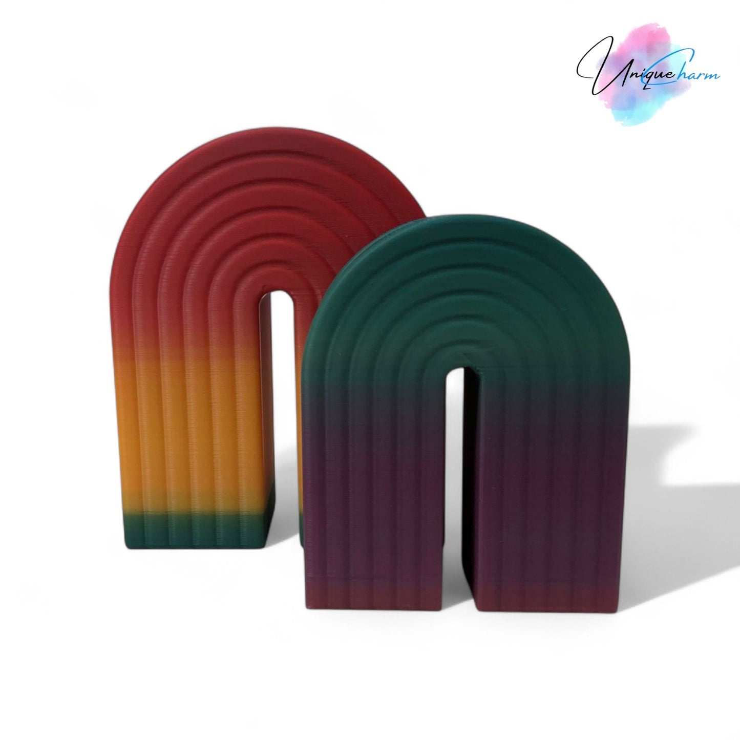 colorful 3d printed rainbow-shaped organizer used as a bookend, pen holder, and mini vase, displayed in two sizes on a shelf with books, stationery, and dried flowers.