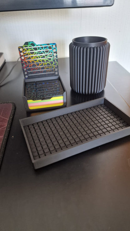 Modern black 3-piece desk organizer set including a ribbed pen holder, textured tray with earbuds case, and sticky notes holder with stencil cards on a black desk.
