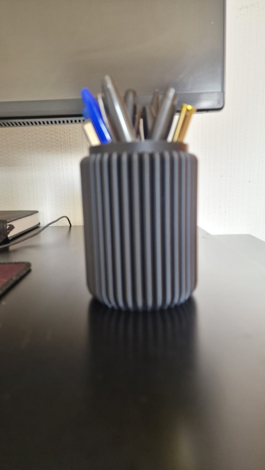 Modern black 3-piece desk organizer set including a ribbed pen holder, textured tray with earbuds case, and sticky notes holder with stencil cards on a black desk.