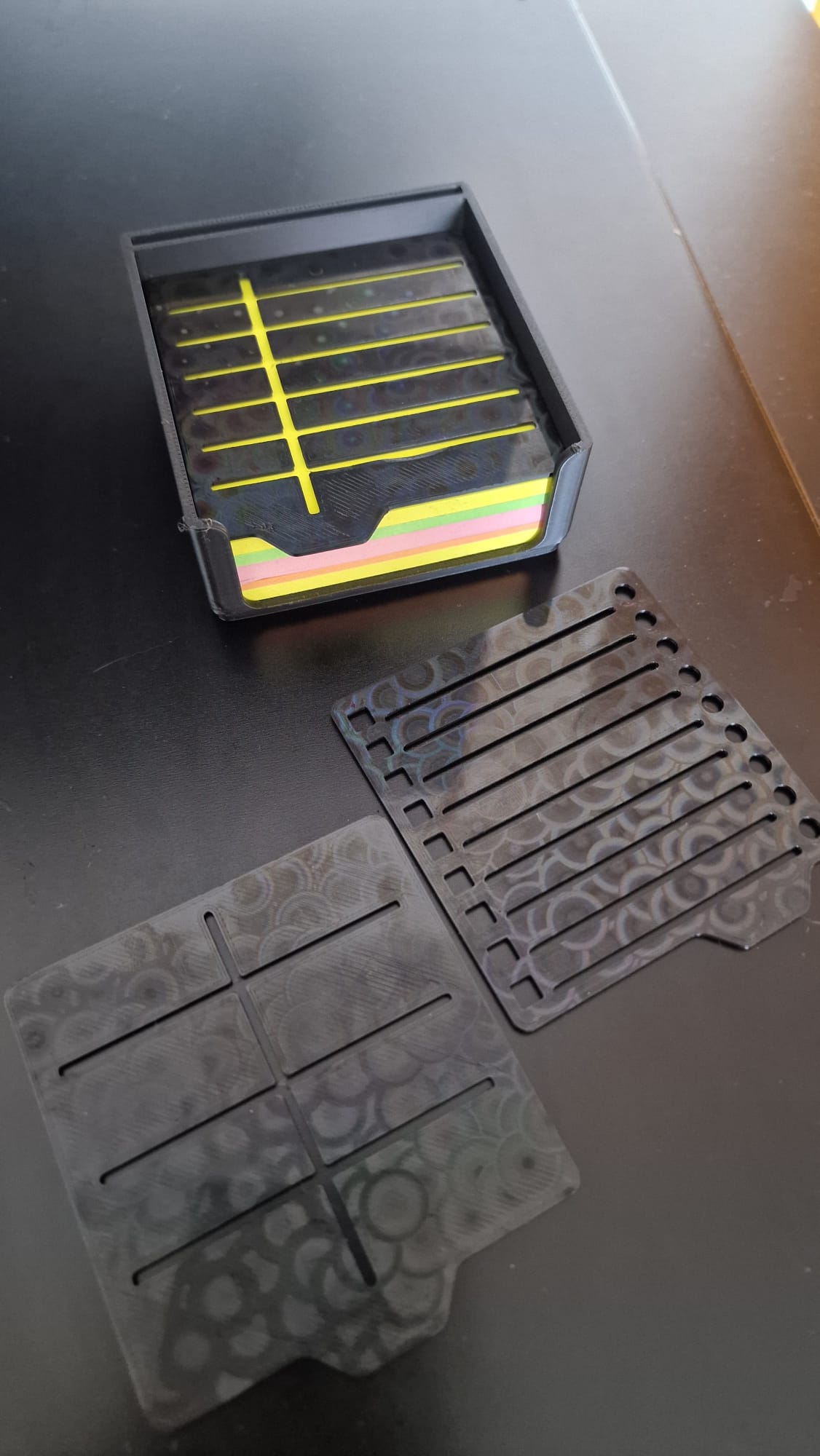 Modern black 3-piece desk organizer set including a ribbed pen holder, textured tray with earbuds case, and sticky notes holder with stencil cards on a black desk.