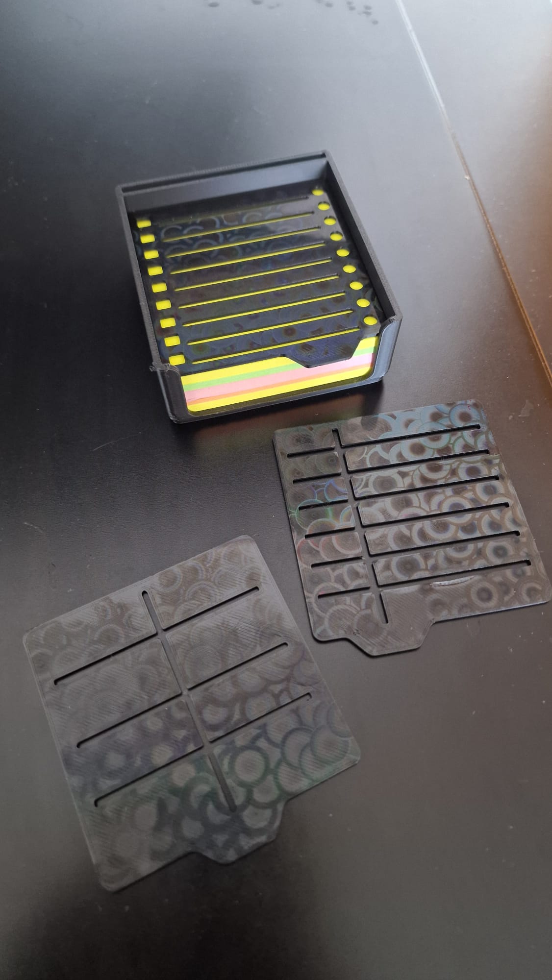 Modern black 3-piece desk organizer set including a ribbed pen holder, textured tray with earbuds case, and sticky notes holder with stencil cards on a black desk.