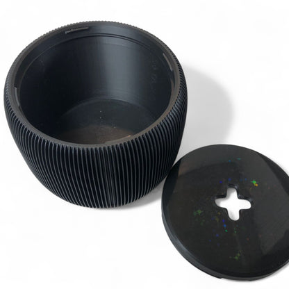 Modern black toilet paper holder with ribbed texture and lid, designed to prevent pets or children from unrolling the paper. Stylish and compact bathroom accessory shown on a white surface.