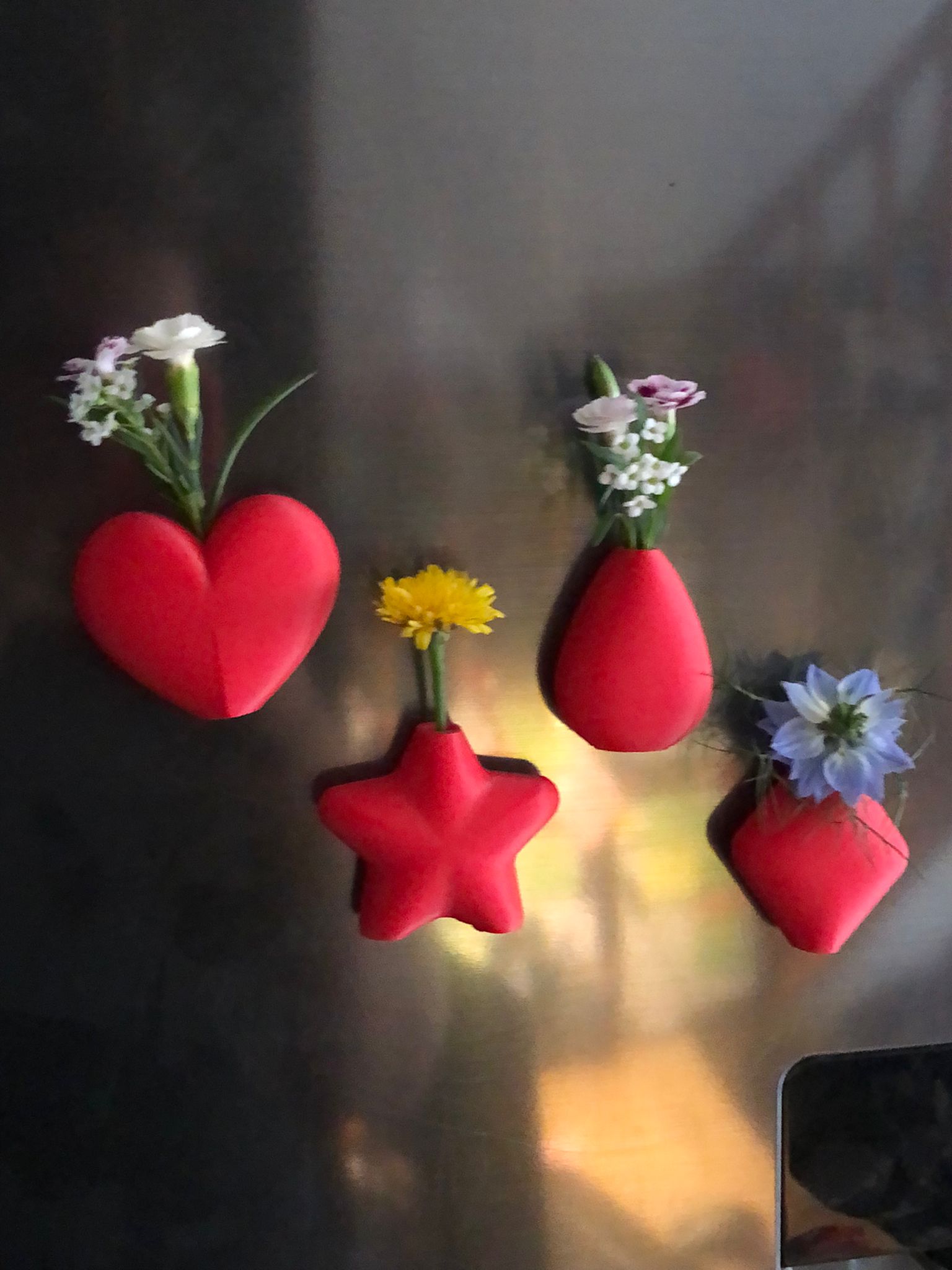 Set of mini magnetic vases in heart, star, diamond, and teardrop shapes, attached to a refrigerator and holding small colorful flowers, displayed in red and white colors.